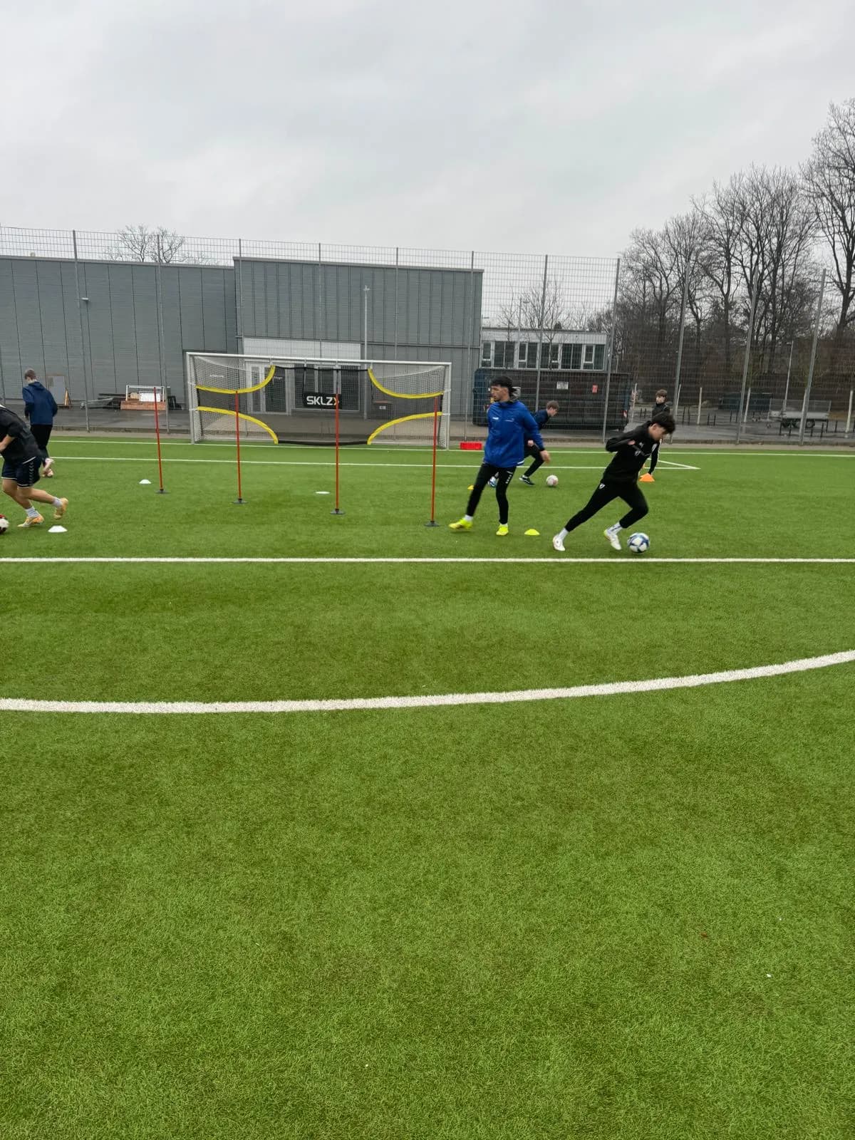 Training auf dem Platz, Oguz in der blauen Jacke zwischen den Spielern.