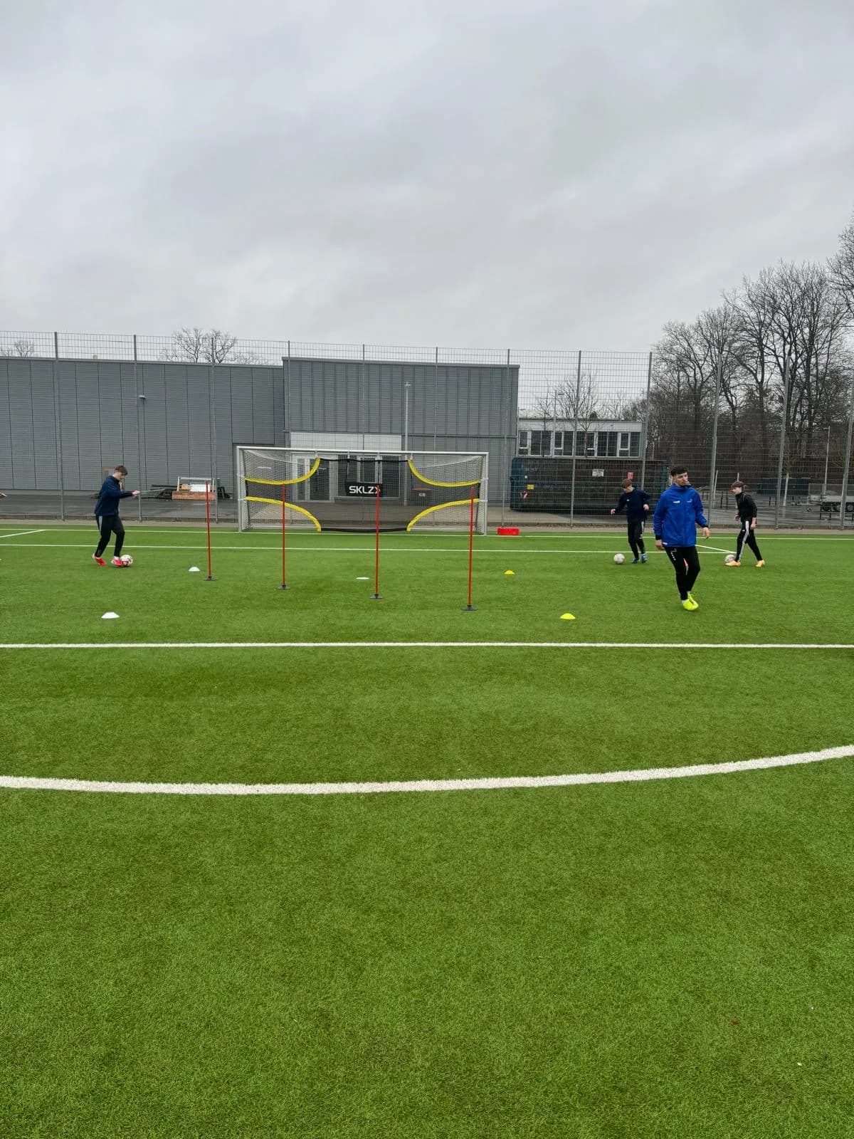 Oguz in der blauen Trainingsjacke auf dem Platz, um ihn herum Spieler bei der Übung.