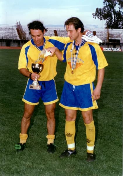 Zwei Spieler in gelb-blauen Trikots mit Pokal und Medaille auf dem Rasen.