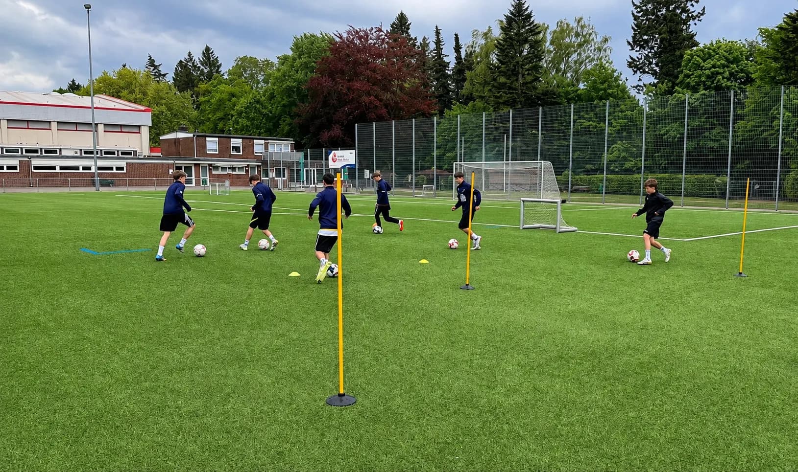 Kinder beim Techniktraining mit Stangen und Bällen im Stadion Reinbek.